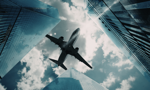 Low-angle view of an airplane flying between glass skyscrapers