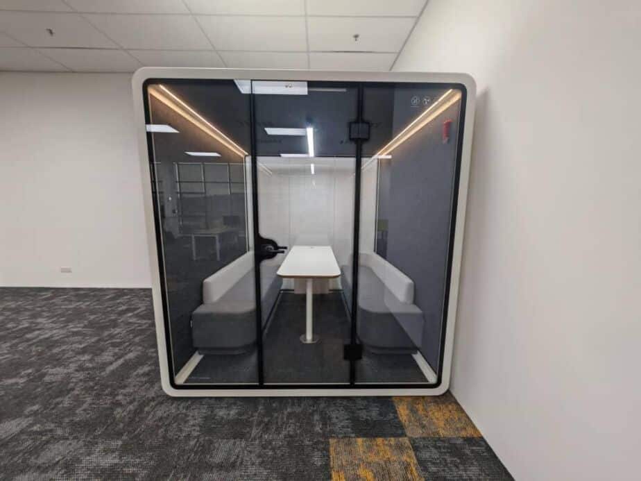 Acoustic booth with sofa seating and a central table, illuminated by warm LED lighting