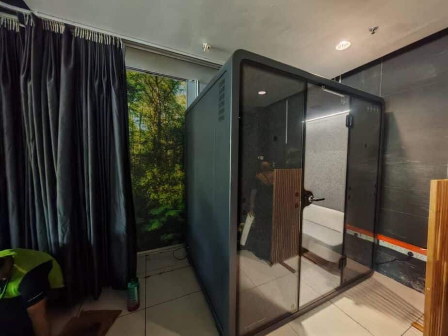 Dark-toned acoustic booth being installed in a room with curtains and a window view of trees
