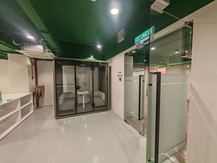 Single-seat acoustic booth in a room with a green ceiling and exit sign