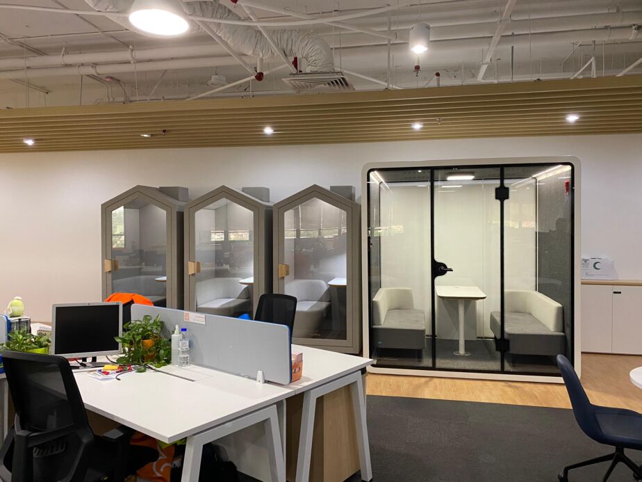 Three pitched-roof acoustic phone booths beside a larger single meeting booth in an office fit-out