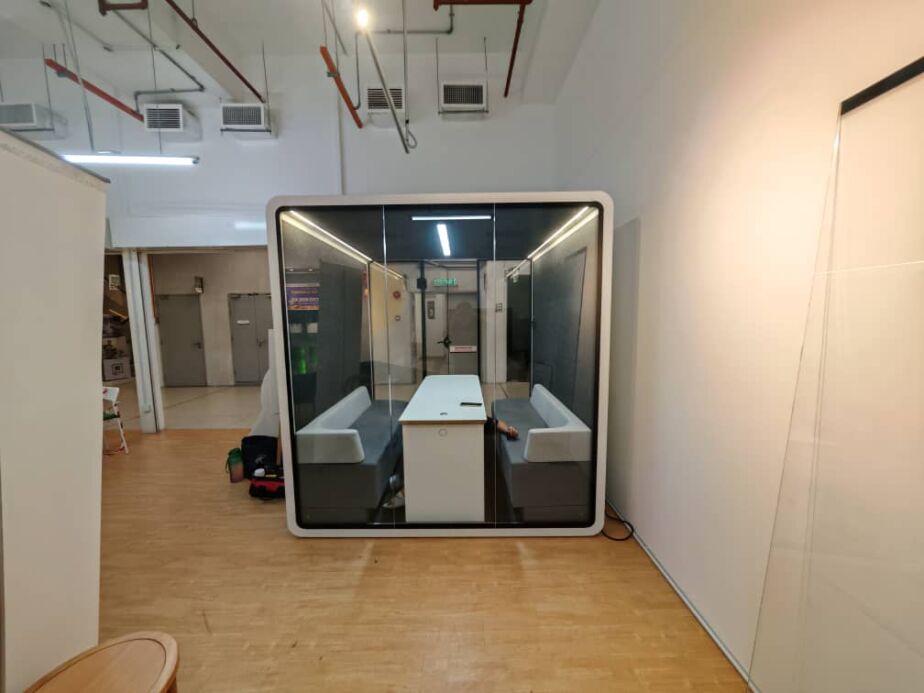 Two-seat acoustic booth with sofas facing a table on a wooden floor