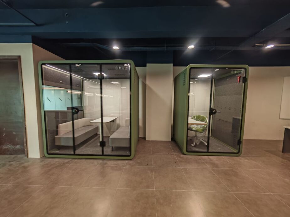 Two olive-green acoustic booths with sofa and single-seat layouts in an office