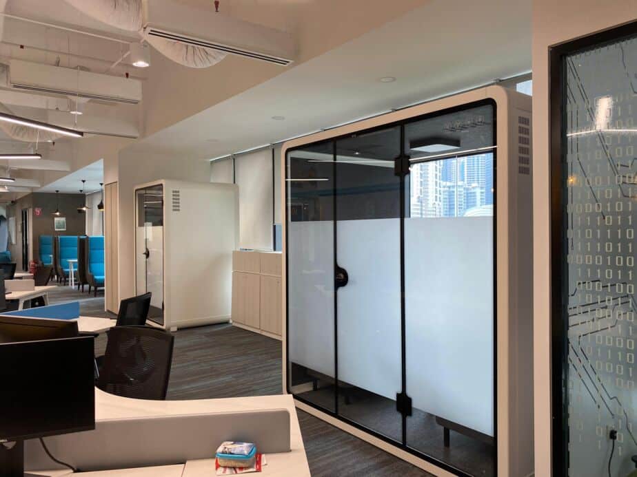 Frosted-glass acoustic booth in an open-plan office with a city view, beside a smaller booth
