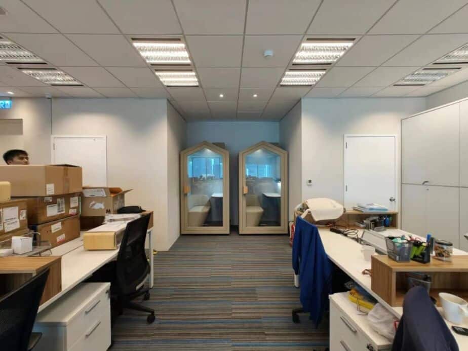 Two pitched-roof acoustic booths built into an office wall between workstations