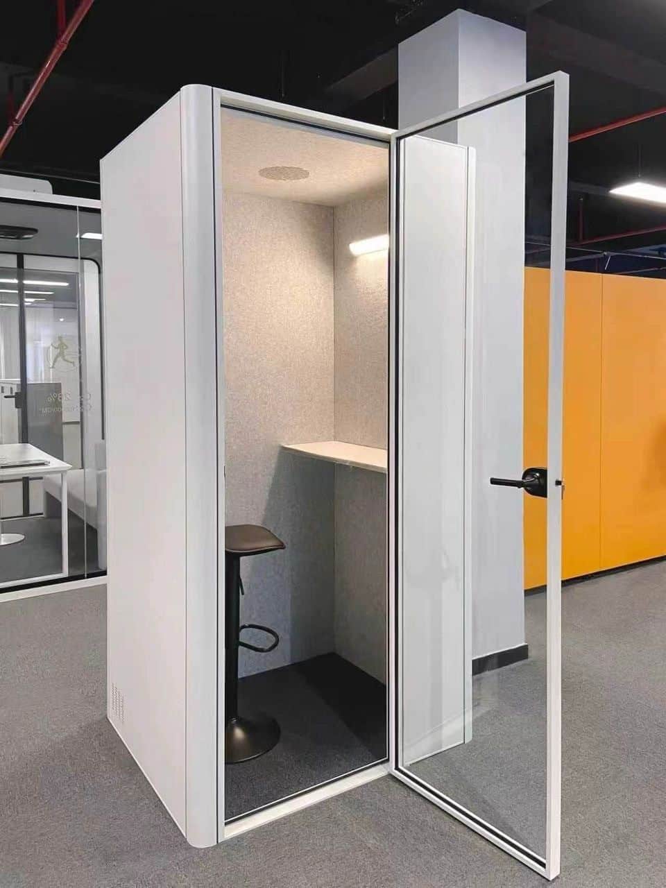 8OOTH acoustic booth installed in an office, door open, showing padded interior with desk and stool