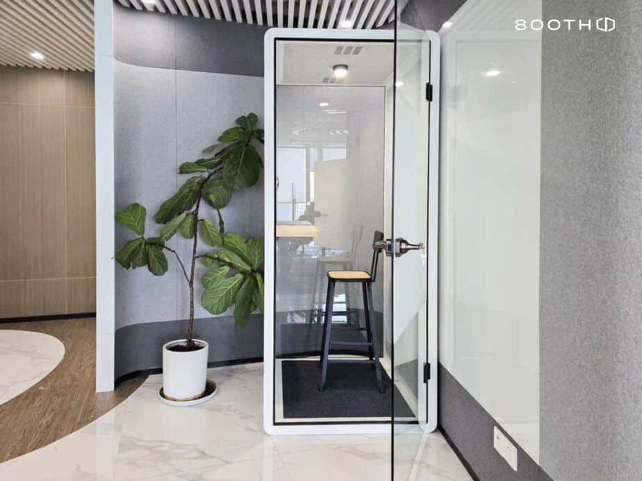 Acoustic booth with a bar stool beside a potted plant, 800TH logo visible on the glass