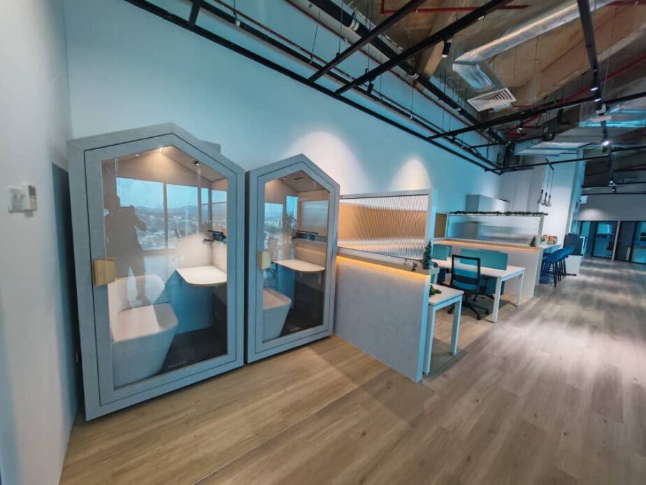 Two pitched-roof acoustic booths in an office beside a standing desk area
